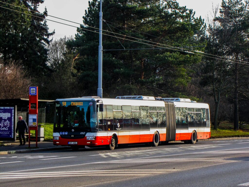Articulated bus at a Prague bus stop during daytime with trees in the background.